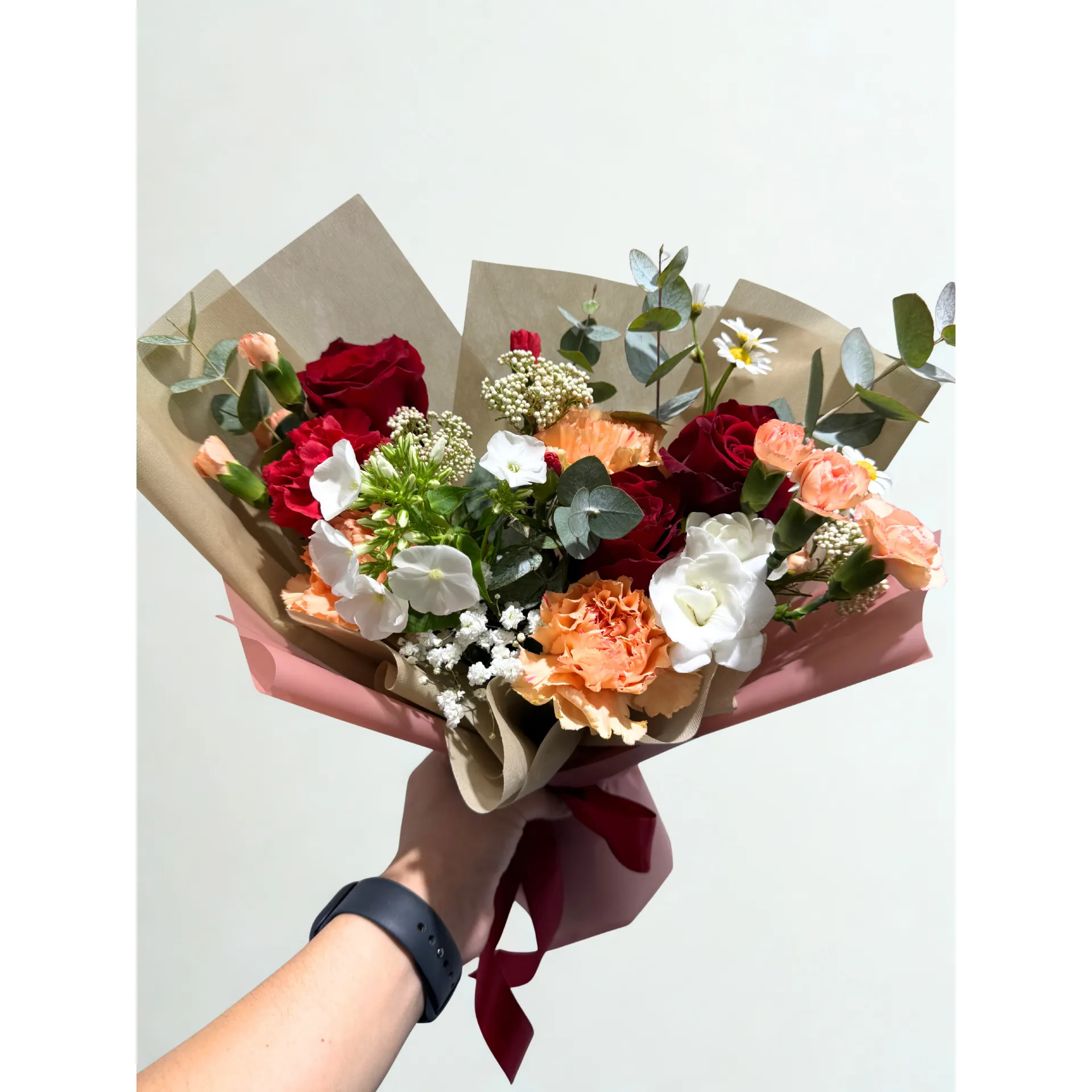 Beautiful hand-tied floral bouquet with red roses, peach carnations, white filler, and eucalyptus